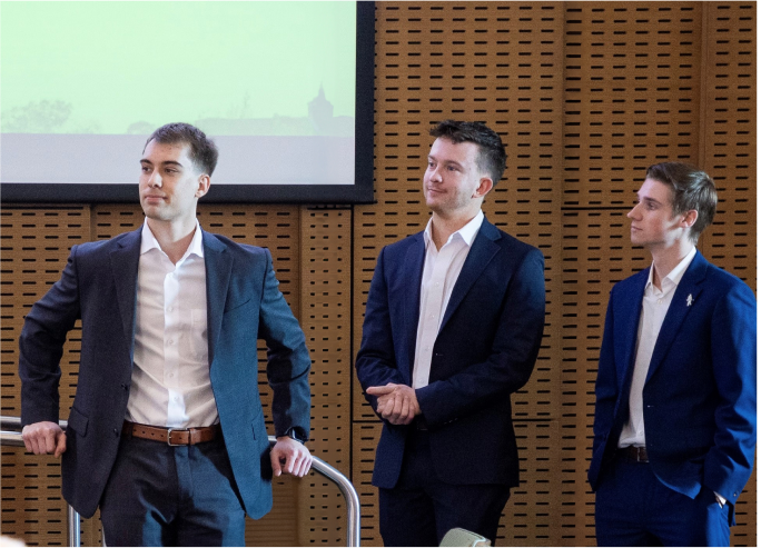 Brite co-founders Nate, Lukas and Craig stand on stage in blue suits during a presentation introducing themselves and the Brite app.