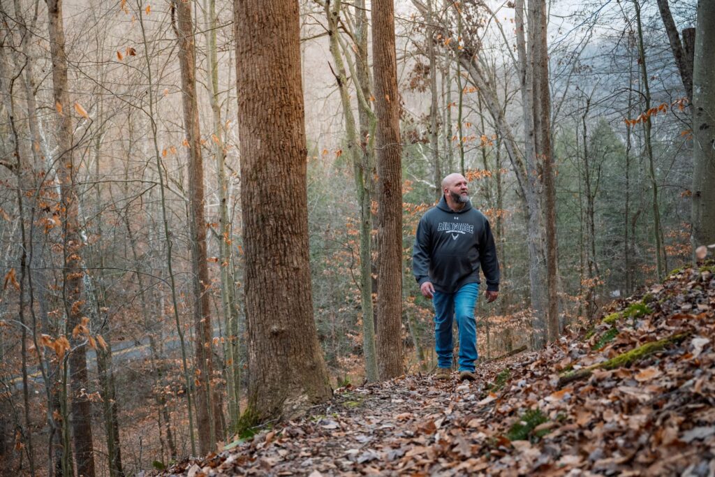 A military veteran wearing a black hoodie and jeans walking in the woods